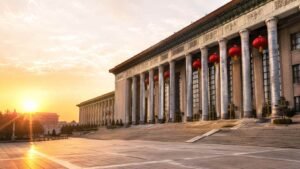 Wide-angle exterior view of the Great Hall of the People in Beijing at dawn with red lanterns, stone steps, and soft golden morning light in a clean editorial news-style scene without people